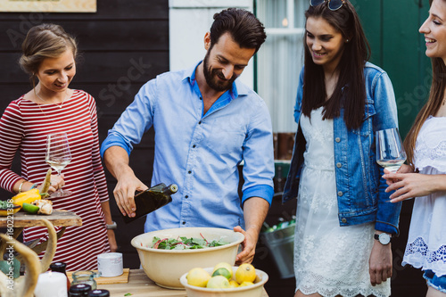 Man pouring olive oil into salad with girls at barbecue outdoors