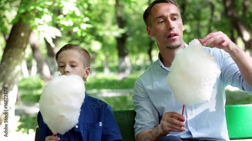 Father and son are resting in the park during the summer holidays and eating sweets