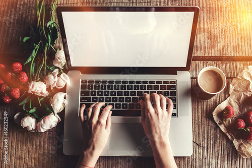 Workspace with girl's hands, laptop computer, bouquet of peonies flowers, coffee, strawberries, smartphone on rough wooden table. Freelancer working in outdoor park. Top view office desk. Flat lay photo