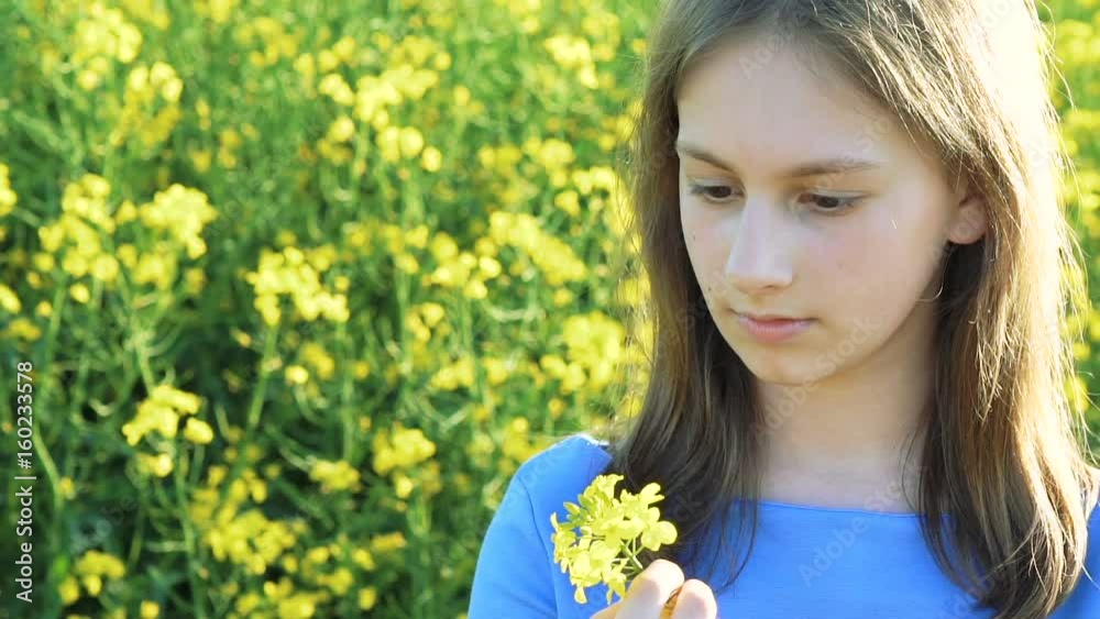 Smart young girl stands with rape flowers and smiling at camera in rape's field Smart young girl stands with rape flowers and smiling at camera in rape's field