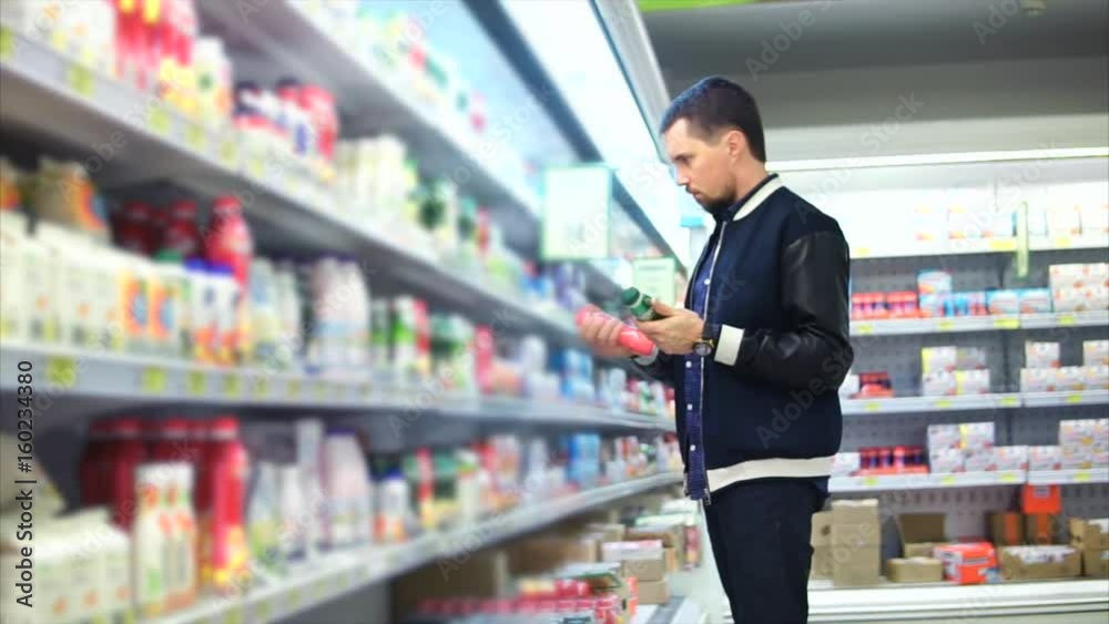An adult man chooses a package of milk in the dairy department of a grocery store, people see plastic cans with pasteurized milk for breakfast