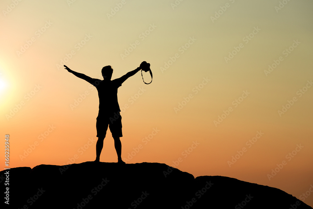 Silhouette of half naked confident man doing a winning pose against the sun on rocky ground Silhouette of half naked confident man doing a winning pose against the sun on rocky ground