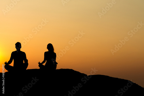 Silhouette of attractive confident half naked man and woman doing yoga on beach rock