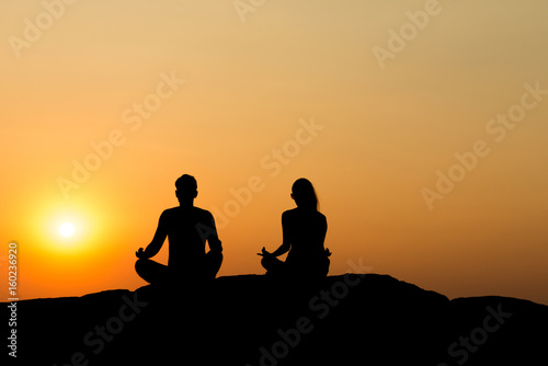 Silhouette of attractive confident half naked man and woman doing yoga on beach rock