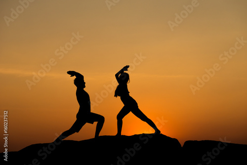 Silhouette of attractive confident half naked man and woman doing yoga on beach rock