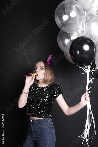 Close up fashion portrait of a young beautiful elegant girl with bright party make up in evening black sequin top. She is keeping silver stars balloons in her hand. Girl at the party. Retouched shot
