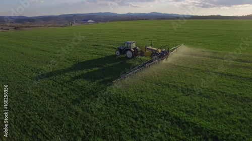 Drone flying over the spraying tractor. The field is like a green carpet.