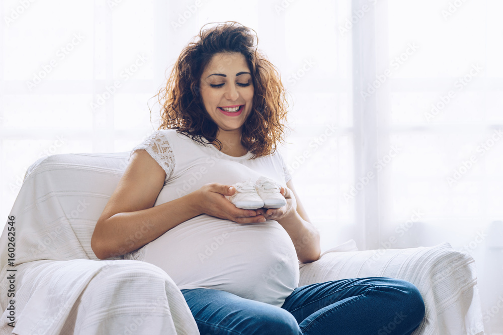 Happy pregnant woman holding baby shoes  in her hands
