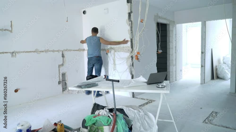 Young man with blueprints measuring wall at new home
Young man with blueprints measuring wall at new home