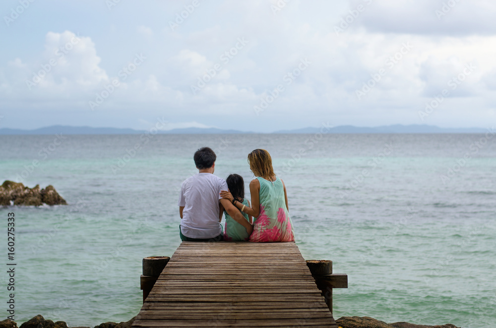 Happy family sitting on wooden walkway looking sea and sky