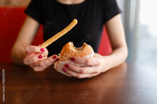 Fast food hamburger and fries in hands in a restaurant on a dish - close-up and focus on the burger