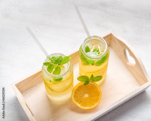 lemonade with fresh lemon and twig mint with drinking straw on wooden tray