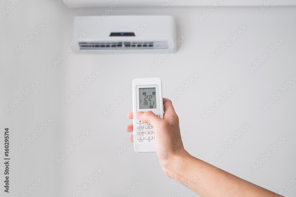 Hand holding remote control, adjusting temperature of air conditioner mounted on a white wall. Indooor comfort temperature Hand holding remote control, adjusting temperature of air conditioner mounted on a white wall. Indooor comfort temperature