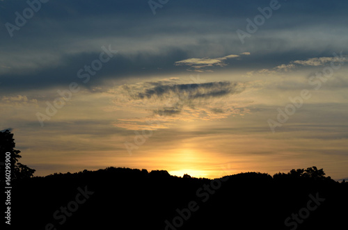 Beautiful sunset over the silhouetted mountains trees © cobracz