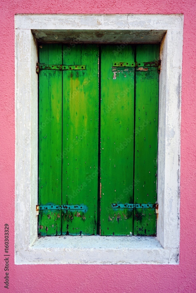 Green window shutters closed on a colorful wall in Burano near Venice, Italy