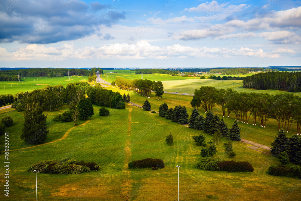 Green fields, meadows, trees, road and blue sky with clouds. Bright summer landscape. Minsk region, Belarus
