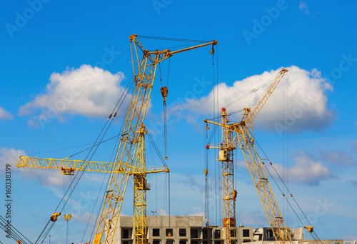 Yellow tower cranes and mobile construction cranes against blue sky background
