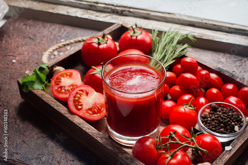 glass of tasty organic tomato juice and fresh tomatoes and herbs on wooden tray in rustic style. Selective focus, healthy lifestyle