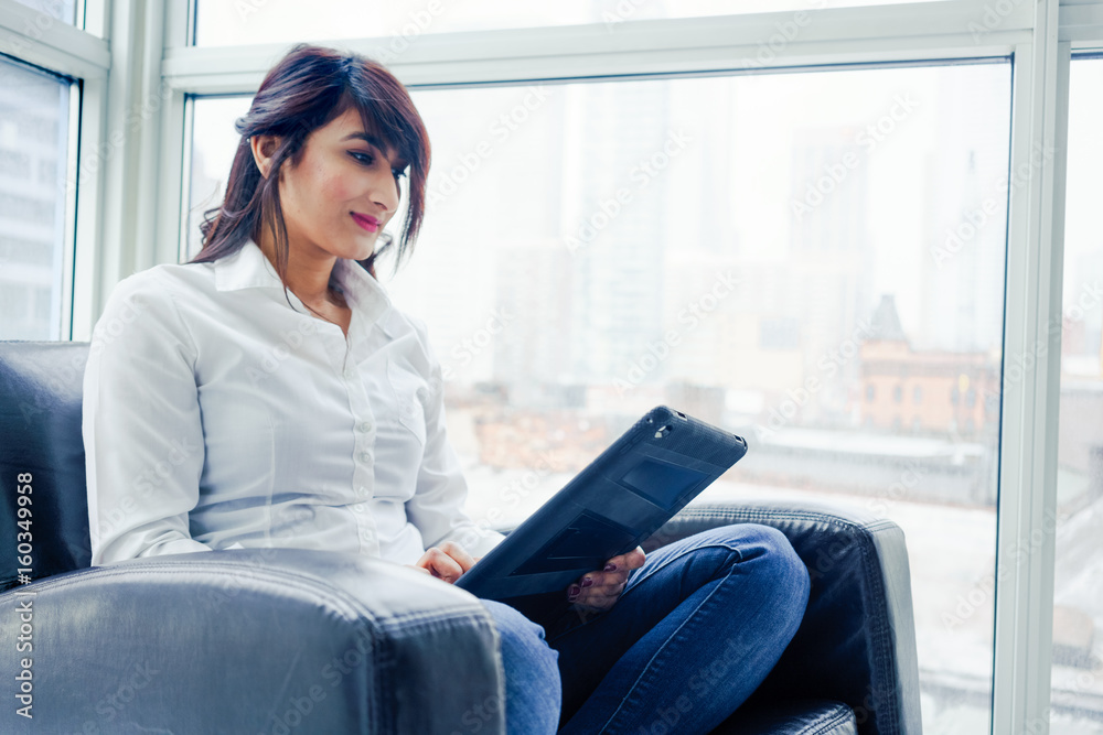 Young woman sitting indoors, in chair using digital tablet, day. Young woman sitting indoors, in chair using digital tablet, day.
