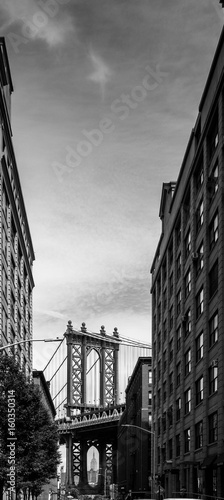 Manhattan Bridge seen through buildings, black and white, New York City, USA.