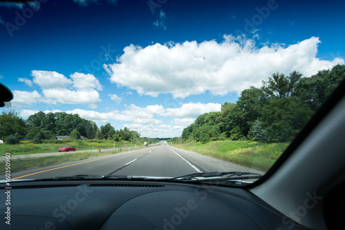 View of main road seen through car windscreen with white clouds in sky.