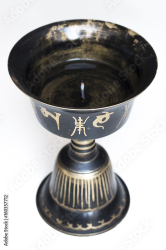 Tibetan buddhist oil lamp close up. Black metal with golden mantras. White background. Religious object.