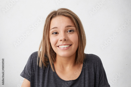 Magnificent pretty woman with dark narrow eyes and pleasant smile shrugging her shoulders having nice and doubtful look while posing against white background. Impressive female with beautiful face