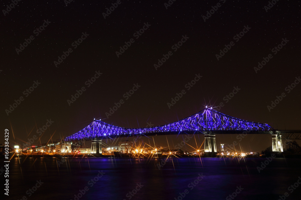 Fototapeta premium Jacques Cartier Bridge Illumination w Montrealu, odbicie w wodzie. 375. rocznica Montrealu. świetlisty, kolorowy, interaktywny most Jacquesa Cartiera. Panoramiczna sylwetka mostu w nocy.
