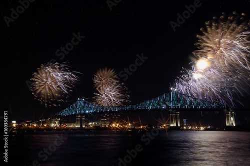 Colorful fireworks explode over bridge, reflection in water. Montreal’s 375th anniversary. luminous colorful interactive Jacques Cartier Bridge. Bridge panoramic colorful silhouette by night.