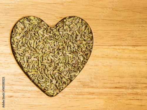 Fennel dill seeds heart shaped on wooden board