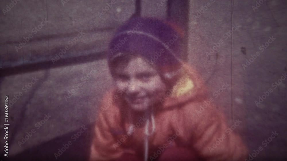 Family chronicle: Little girl child play on playground near home. Her father is recording video on 8 mm retro camera. Daughter looking at camera smiling and winking to father.