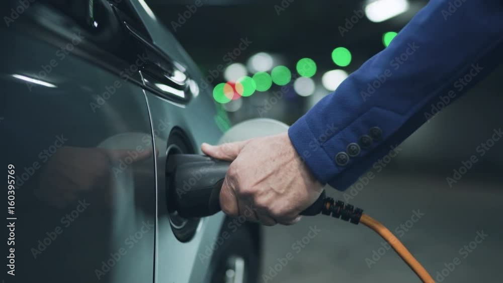 Senior is plugging in power cord to an electric car. Close up. 4K Senior is plugging in power cord to an electric car. Close up. 4K