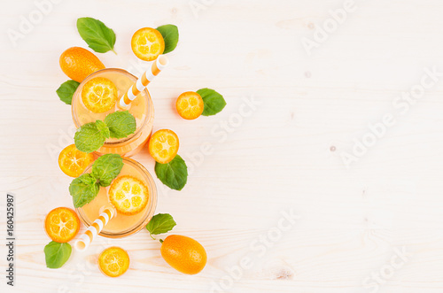 Decorative frame of orange citrus kumquat fruit smoothie in glass jars with straw, mint leaf, cute ripe berry, top view. White wooden board background, copy space.