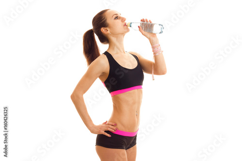 Slim fitness girl stands sideways in the Studio and drinking water from a bottle