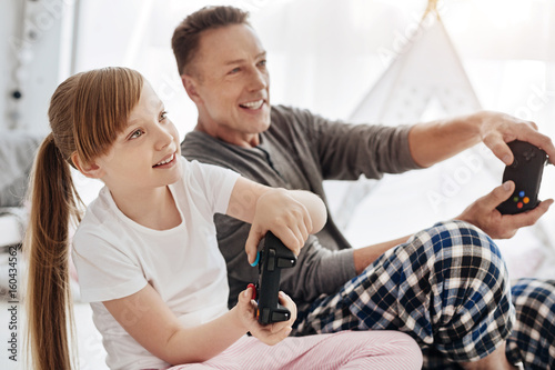 Engaged emotional child and her father using controllers for playing