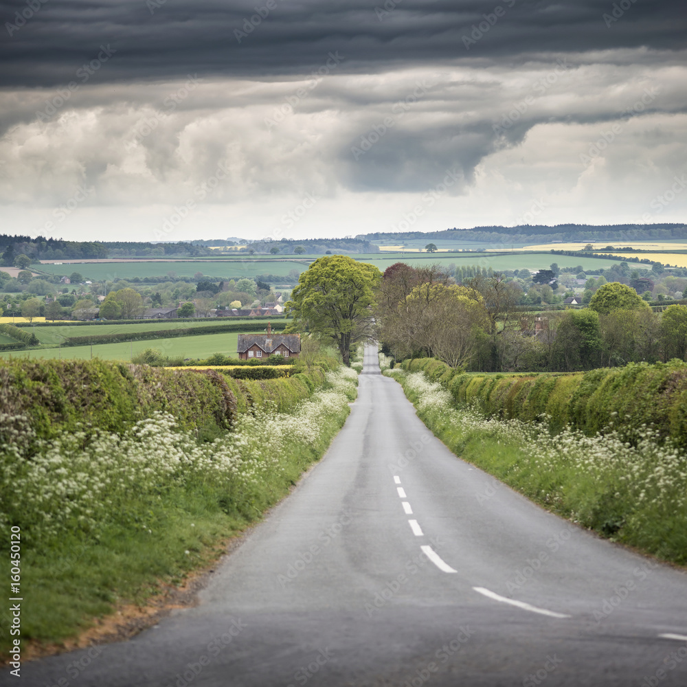 Landscape image of empty road in English countryside with dramatic stormy sky overhead