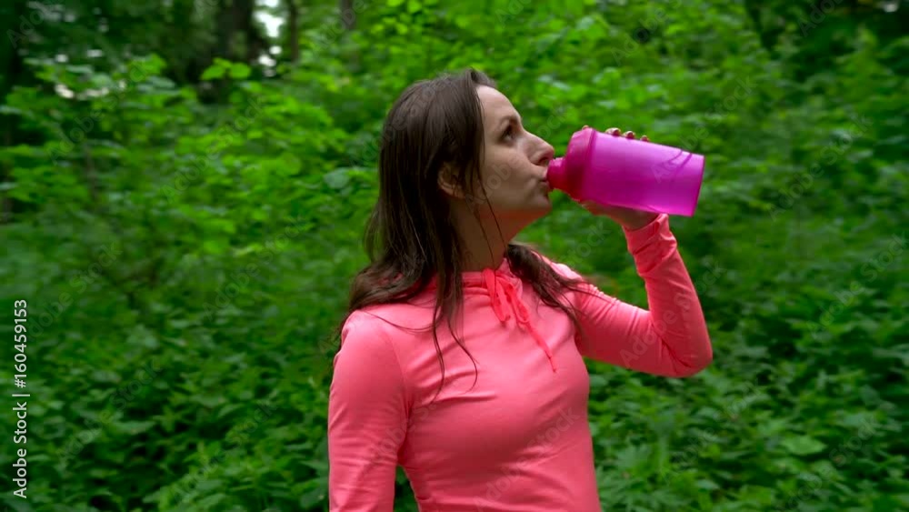 Woman drinking water and resting while jogging in the forest Woman drinking water and resting while jogging in the forest