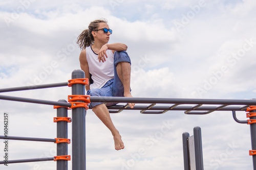 Teenager with dreadlocks sits on the bar on the playground