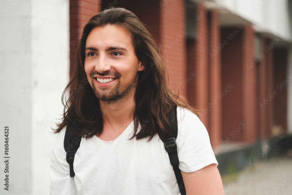 Stylish hipster model with long hair lifestyle in the street. Dressed in a white T-shirt and torn blue jeans in the city Stylish hipster model with long hair lifestyle in the street. Dressed in a white T-shirt and torn blue jeans in the city