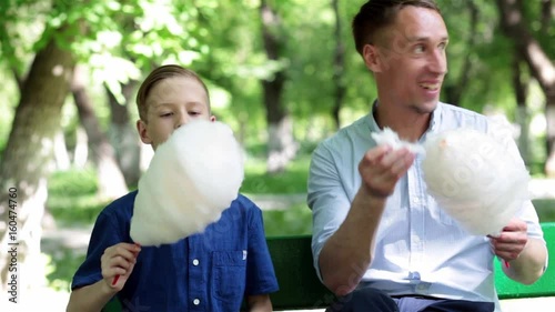 Father and son are resting in the park during the summer holidays and eat sweets, play in nature