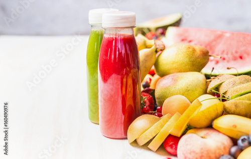 Bottles with red smoothies and juices beverages on white table background with summer fruits and berries, front view. Healthy food and vegetarian eating concept