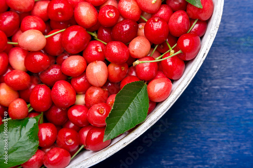 Red cherries in white basket on blue wooden background. Cherry close up. Top view.