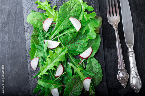 Mixed salad leaves with radish on black slate plate. Top view.