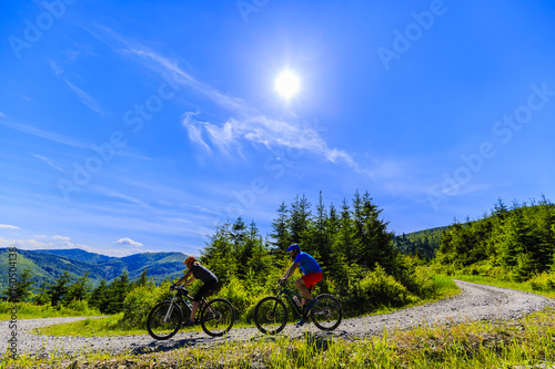 Mountain biking women and man riding on bikes in summer mountains forest landscape. Couple cycling outdoor sport activity.