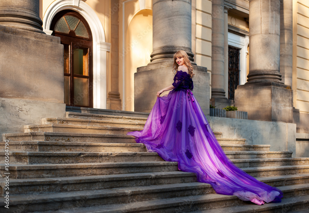 blonde girl in violet dress with  plume stending on stairs of a castle