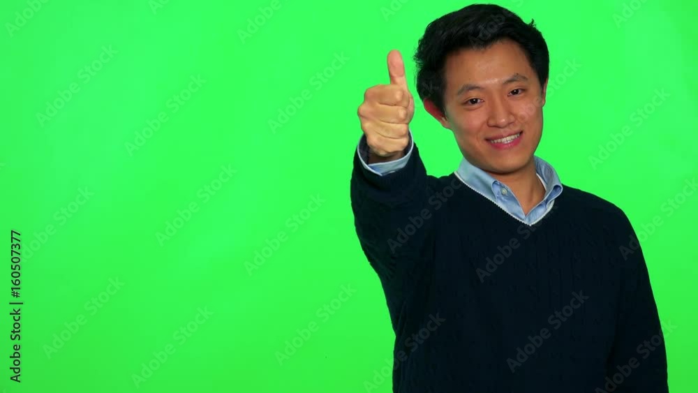 A young Asian man smiles and shows a thumb up to the camera - green screen studio A young Asian man smiles and shows a thumb up to the camera - green screen studio
