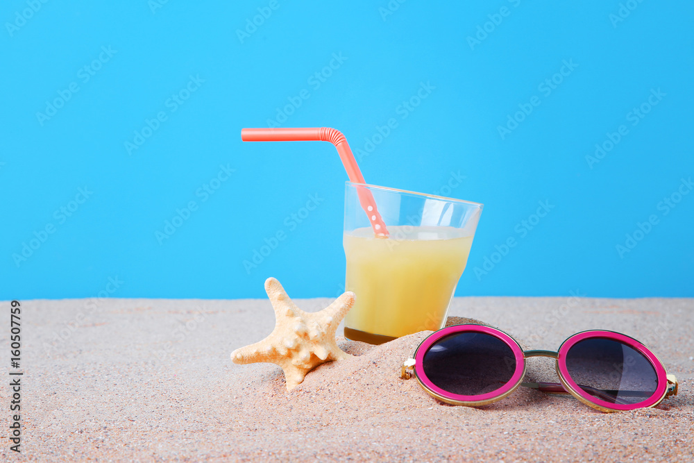 Pink sunglasses with glass of juice and starfish on the beach sand