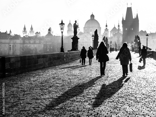 Foggy morning on Charles Bridge, Prague, Czech Republic. Sunrise with silhouettes of walking people, statues and Old Town towers. Romantic travel destionation. Black and white image.