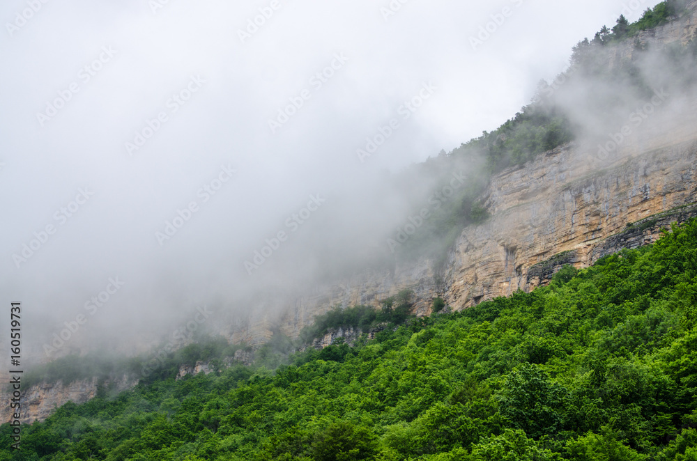 Haze fog over the rocks. Cloud over the mountainin Caucasus. Green leaf forest. Mezmay and Guamka