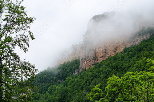Haze fog over the rocks. Cloud over the mountainin Caucasus. Green leaf forest. Mezmay and Guamka